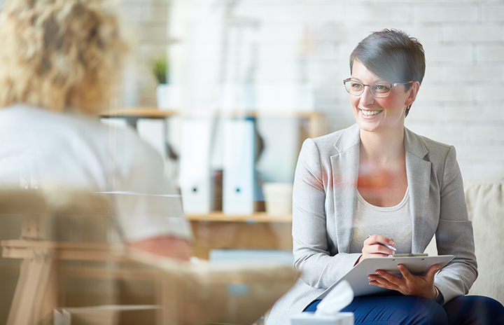 A professional in a grey jacket taking some notes and talking to a patient; office
